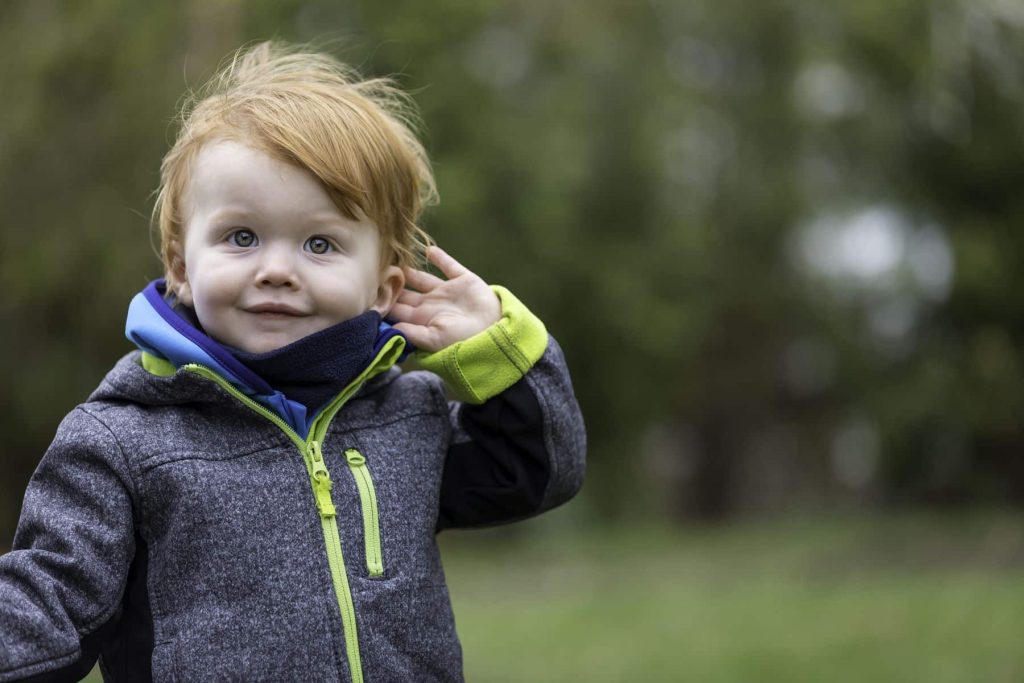 little boy with red hair holding his hand up to his ear
