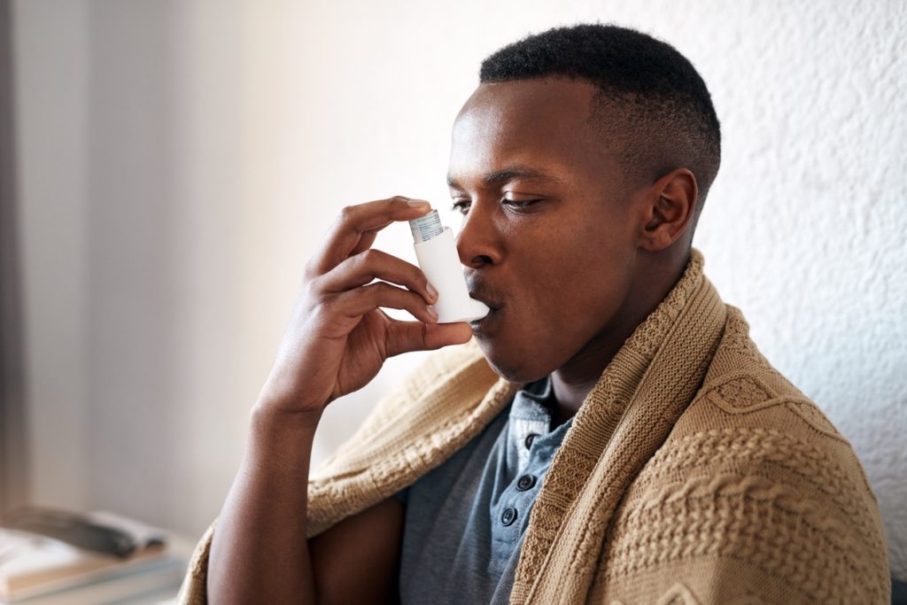 A man in a brown sweater using an asthma inhaler.