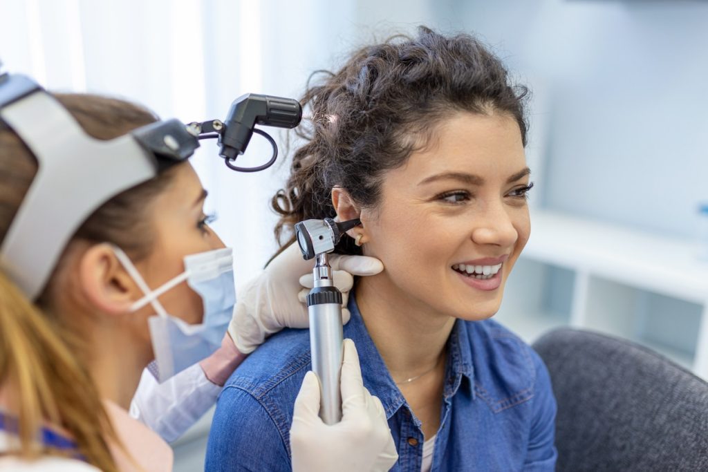 A young woman during an ear check-up with an audiologist with an otoscope in her ear