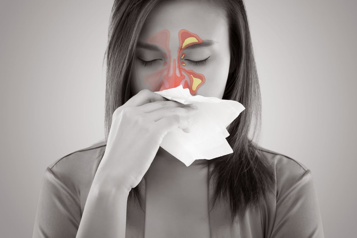 A black and white photo of a woman with sinus pain holding a tissue and red lights lighting up the inflammation.