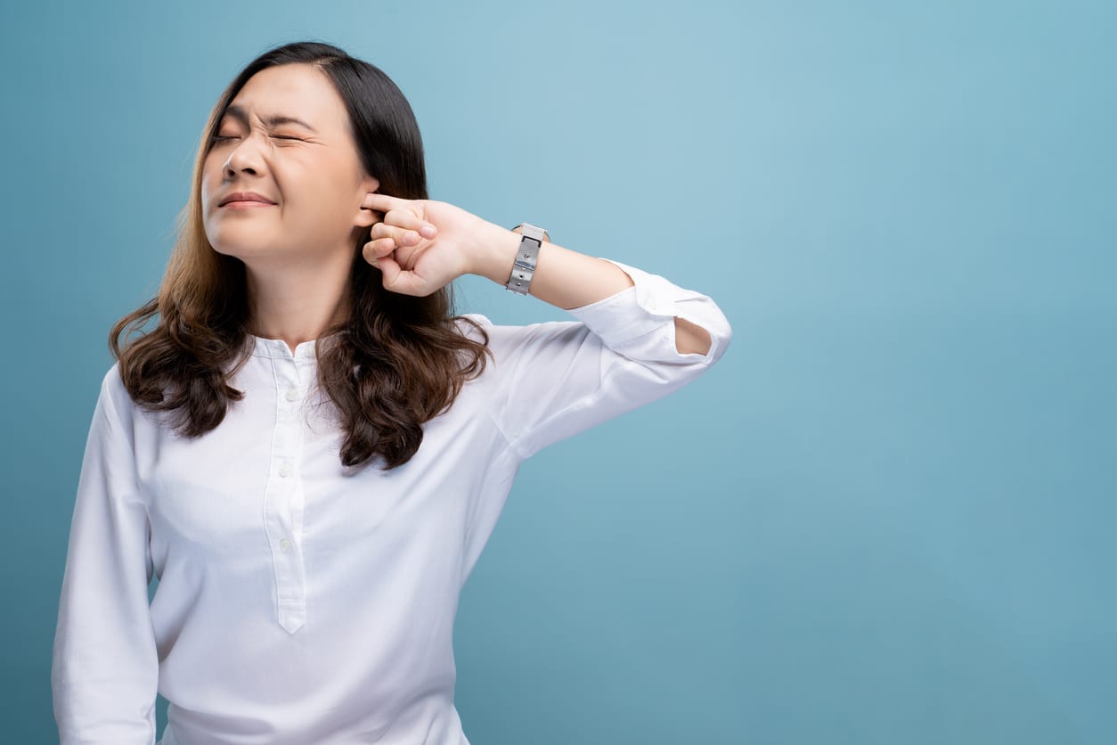 A woman in a white shirt putting a finger into her ear, representing clogged ears.