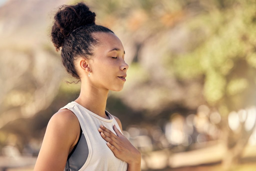 A woman outside breathing deeply with her hand over her chest.