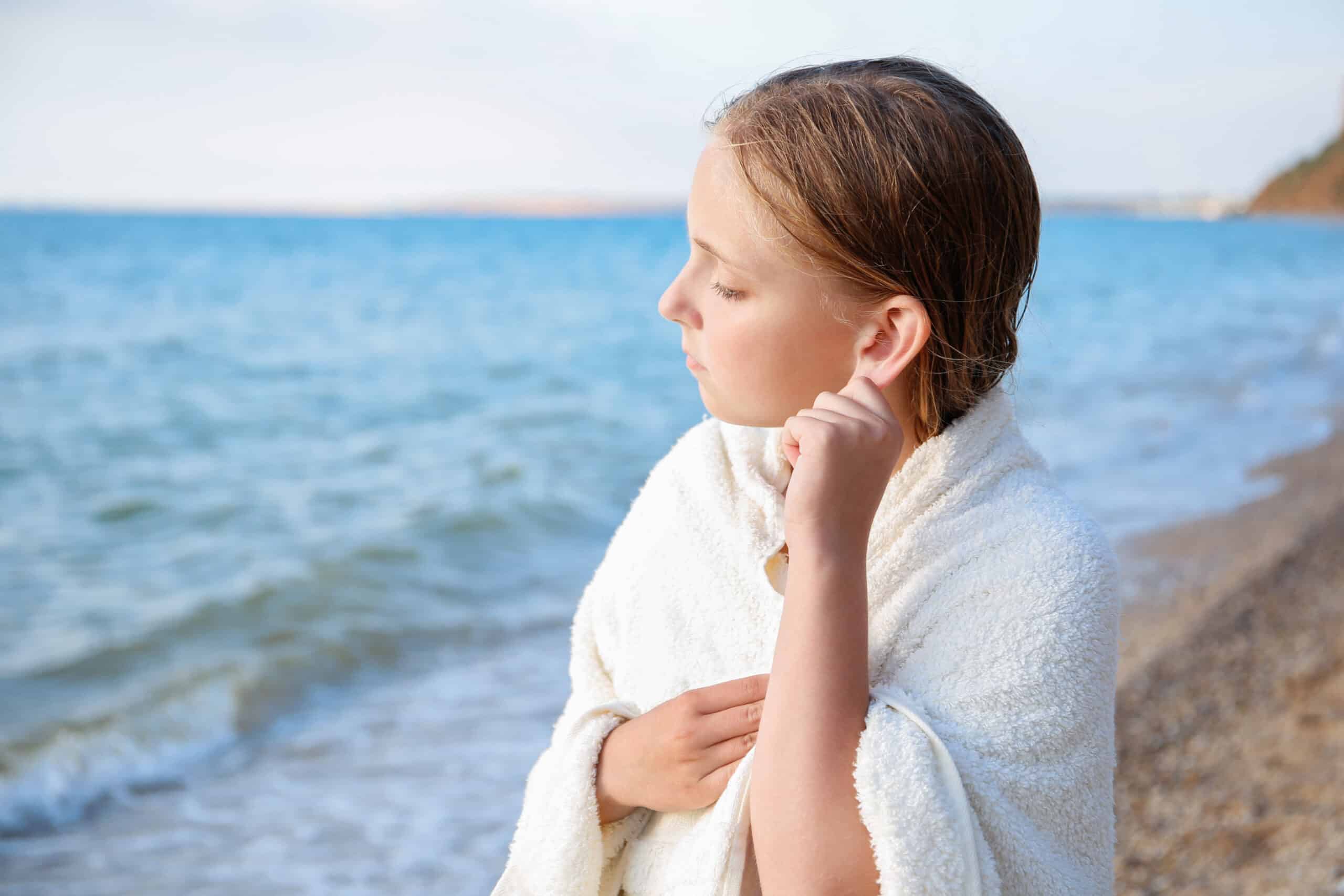 A young girl at the beach tugs at her ear. Swimmer’s ear is a common water-related ear issue.
