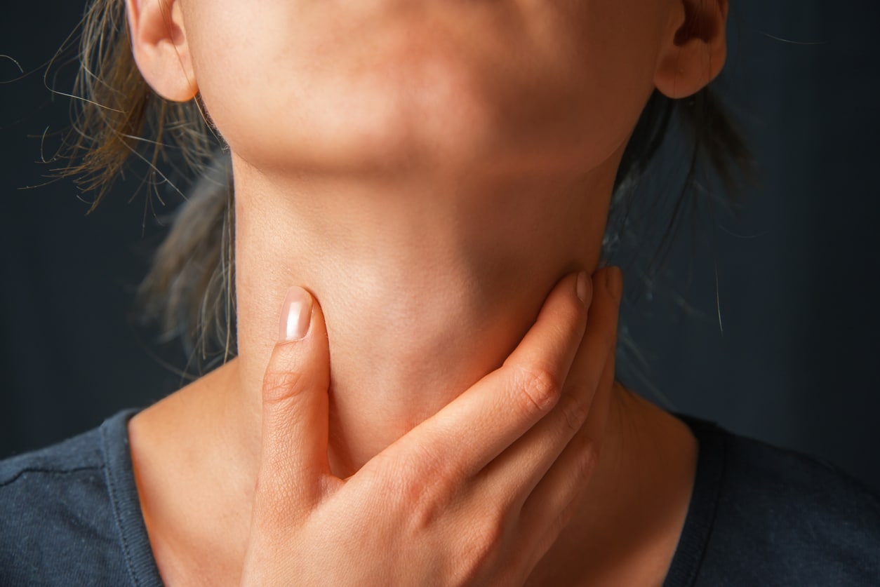 A woman with her hands on her neck shows discomfort associated with globus sensation.