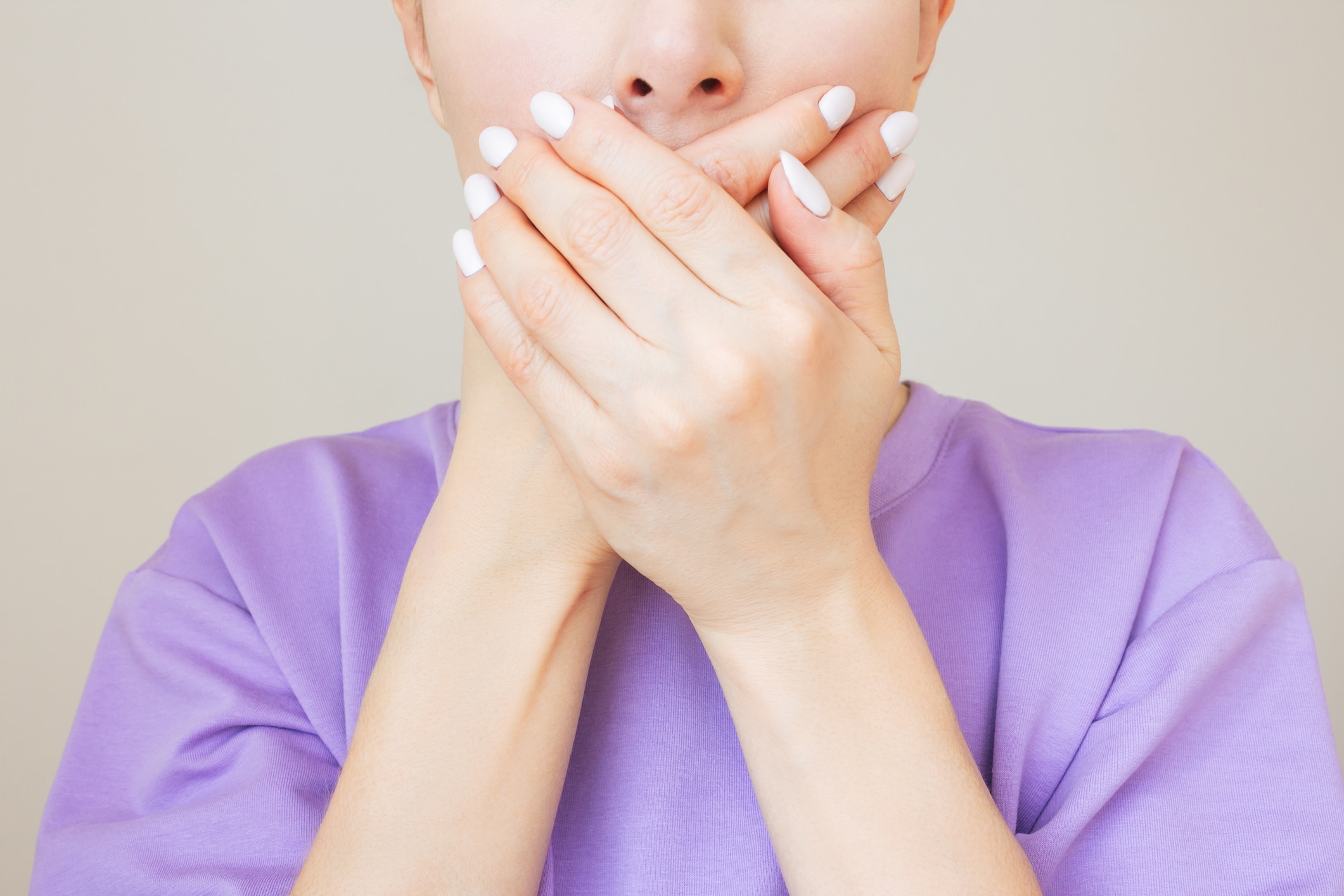 A woman covers her mouth with her hands, concerned about halitosis and its potential ENT connections.