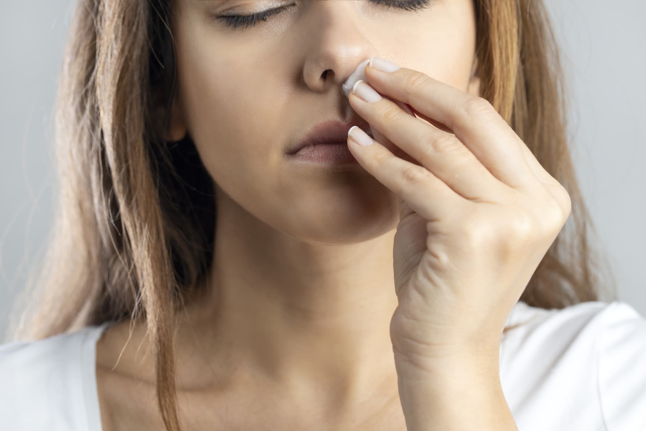 A woman experiencing multiple nosebleeds a week holds a tissue to her nose to stop the bleeding.